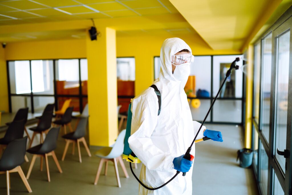 Contractor disinfecting office for COVID-19 coronavirus. A disinfector in a protective suit and mask